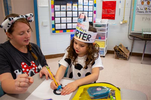 teacher helping student wearing a paper hat
